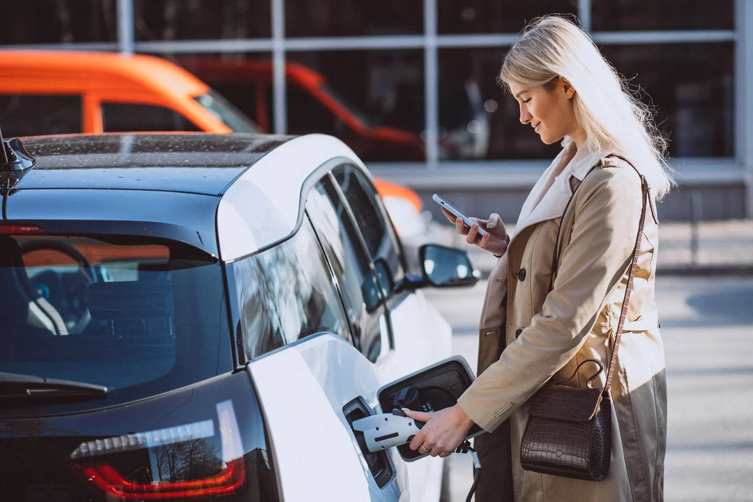 a women is charging his cars while using mobile